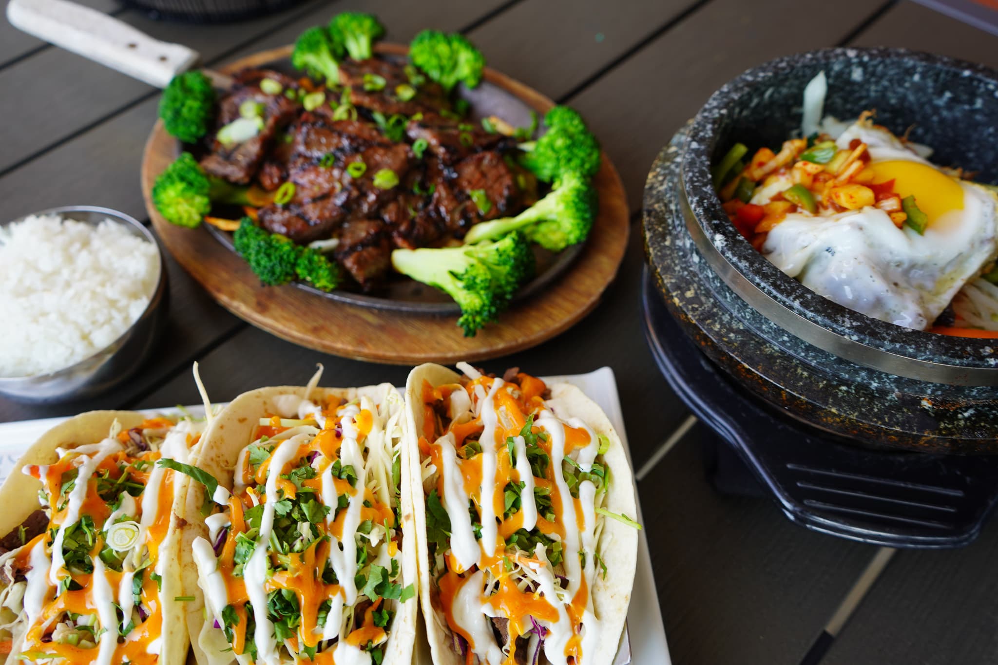 A Seoul Kitchen table spread: kalbi on a sizzling platter, stone pot bibimbap, and Korean tacos