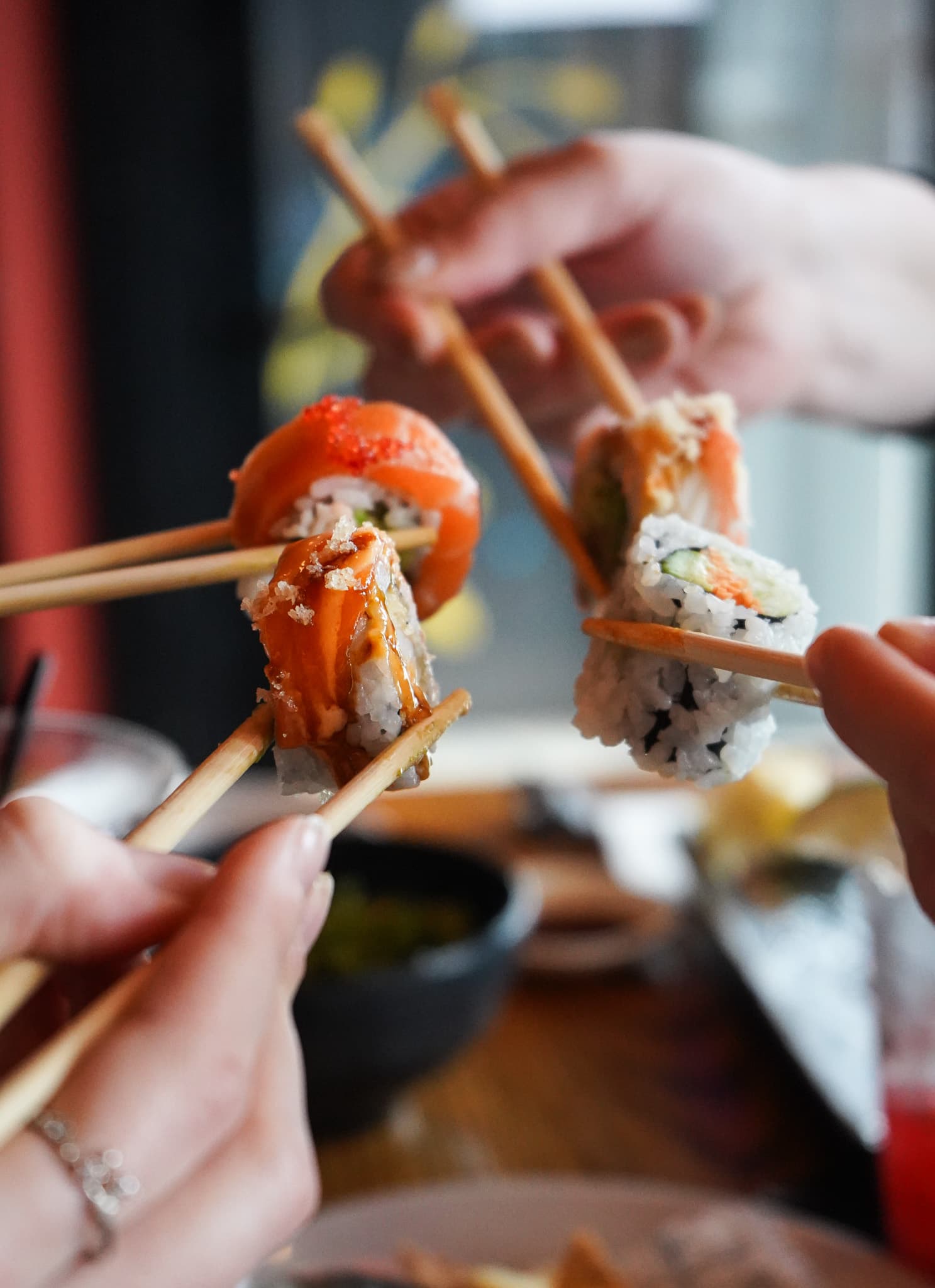 Friends toasting with pieces of sushi held in chopsticks